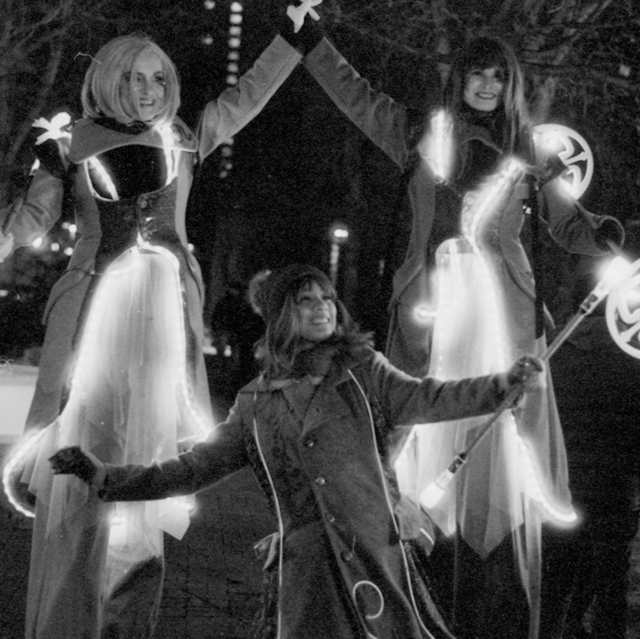 A black and white photo of 3 women look happily while dressed in LED outfits